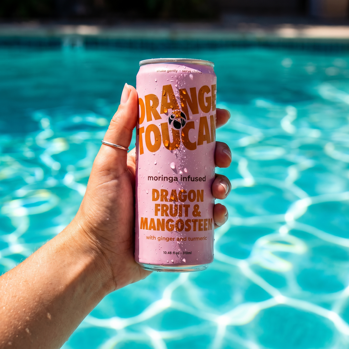 A hand holding a can of Dragon Fruit & Mangosteen over a pool