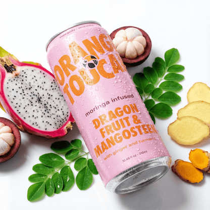 Pink can of Orange Toucan dragon fruit and mangosteen drink with dragon fruit, mangosteen, ginger, and tumeric on a white background surrounded by the ingredients