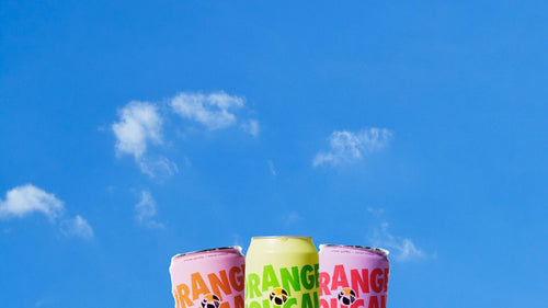 Three colorful cans of Orange Toucan against a blue sky with white clouds.
