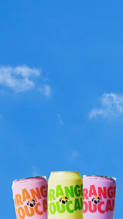 Three cans of Orange Toucan against a blue sky with white clouds