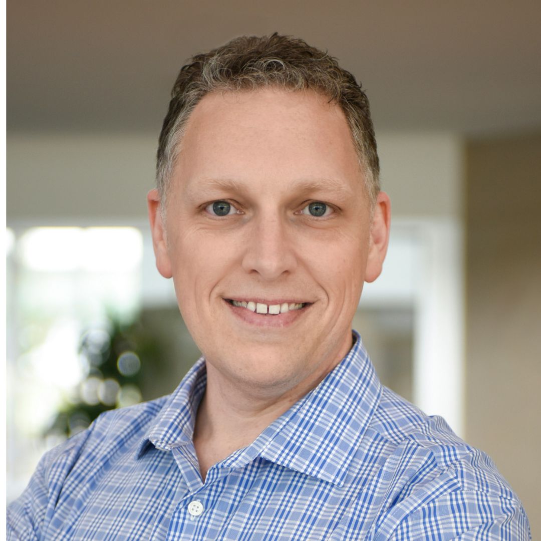 Man wearing a blue plaid shirt with a blurred indoor background