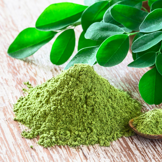 Green moringa powder on a wooden surface with fresh green moringa leaves