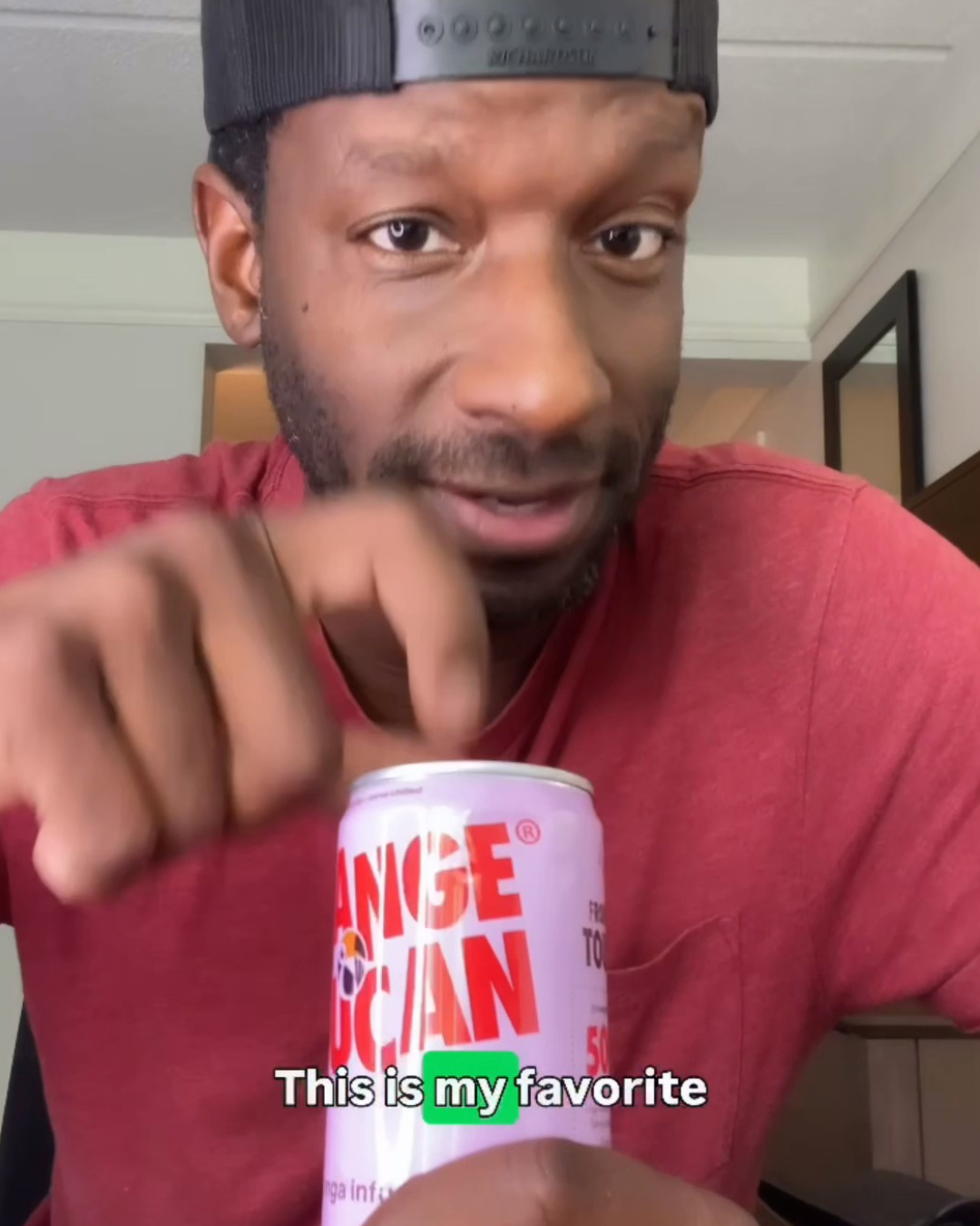 Man holding a can of Orange Toucan with text 'This is my favorite' in an indoor setting.