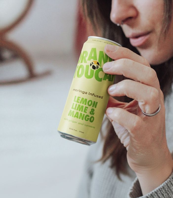 Person holding a can of moringa infused Orange Toucan lemon lime mango drink, containing giner and turmeric